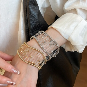 Detail of woven metallic open cuff bracelet in gold and silver finish on model wrist