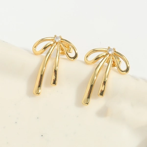 Detailed view of golden bow earrings with a central clear zircon stone on a minimal base