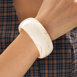 Detail of wide resin bangle with creamy marble pattern worn over a checkered blazer
