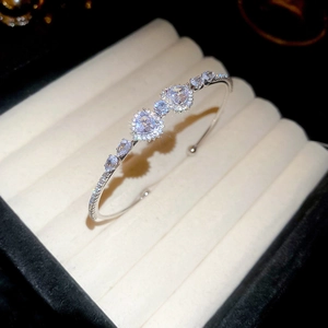 Close-up of luxury silver open bangle with heart and teardrop zircon on velvet pad