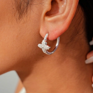 Macro shot of silver flower hoop earring with sparkling zircons on a female ear