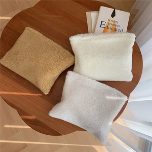 Three plush lamb wool makeup bags in camel, cream, and white on a wooden table