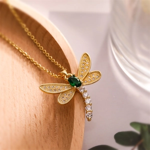 Macro shot of gold dragonfly pendant with green gem and white zircon detail work