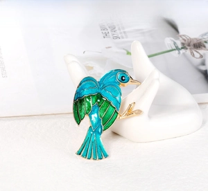 Detailed view of bird brooch featuring green enamel wings on golden metal base