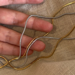 Minimalist gold and silver layered snake chain necklaces shown on a textured fabric