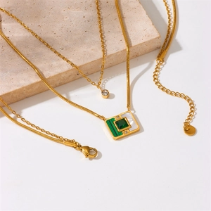Detail of layered gold necklace featuring round clear gem and vintage square green pendant