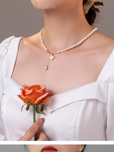 Detailed close-up of a pearl necklace with heart pendant and teardrop pearl on a model