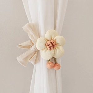 Detail of beige fabric flower curtain tieback with pink pom-poms and bow on white curtain