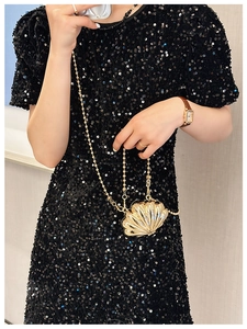 Close-up of golden shell-shaped metal mini bag with chain strap held by a model
