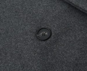 Detail eines schwarzen Marmorknopfes auf dem dunkelgrauen Wollstoff des Mantels