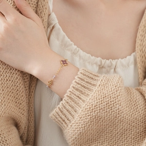 Detail view of a vintage gold clover bracelet with beads worn on a beige knit sleeve