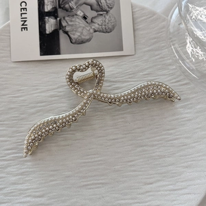 Dettaglio macro della pinza per capelli a cuore dorata con perle e strass su vassoio