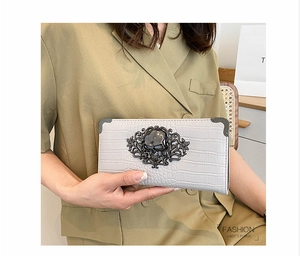 Detail of light grey crocodile pattern evening clutch featuring a black metal skull