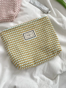 Macro view of a bubble-knit blue and yellow makeup bag on a white textured background