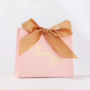 Detail of pink wedding favor box with gold Thank You text and champagne ribbon bow