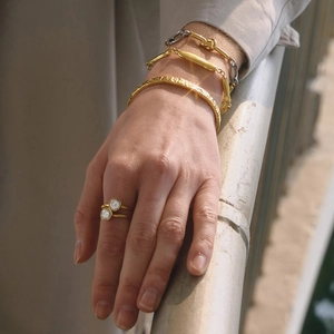 Close-up of stacked gold stainless steel bracelets and double-stone ring on model's hand