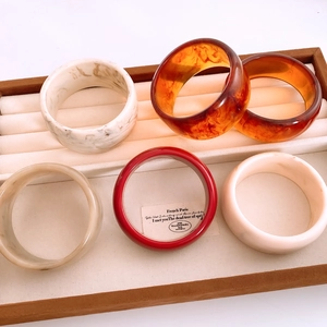 Collection of wide resin bangles in marble, amber, and cream finishes on a display tray