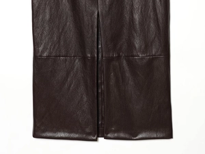 Dettaglio di una gonna in pelle marrone scuro con spacco laterale e trama premium