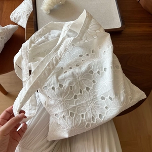 Detailed close-up of white cotton tote bag with intricate floral embroidery and cutouts