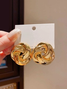 Macro detail of large gold twisted knot earrings on a white display card holder