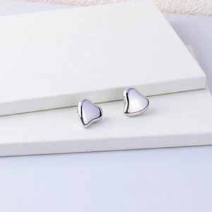 Polished silver heart stud earrings in 18K gold plated stainless steel on white steps