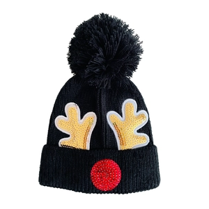 Close-up of black knit beanie with golden sequin reindeer antlers and red nose detail