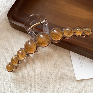 Detailed close-up of amber resin hair claw clip with golden spring on textured fabric