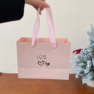 Close-up of pink paper gift bag with silk handles and LOVE text for necklace packaging