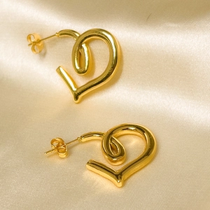 Macro shot of minimalist gold heart-shaped stud earrings on a luxury silk fabric background