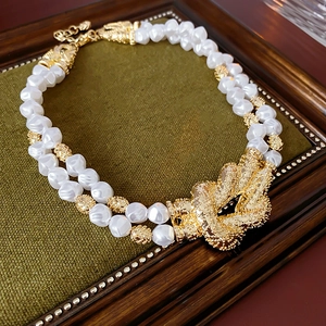 Close-up of double-layer pearl necklace with vintage gold knot pendant on green velvet