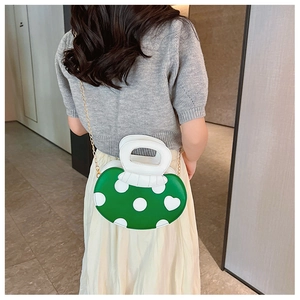 Green mushroom-shaped crossbody bag with white dots and gold chain strap on model