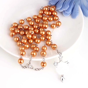 Chapelet de perles orange avec croix en argent sur une assiette en céramique