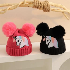 Nahaufnahme von Strickmützen mit flauschigen Doppelbommeln und Einhorn-Stickerei