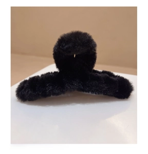 Détail d'une pince à cheveux en peluche noire douce sur socle minimaliste pour l'hiver
