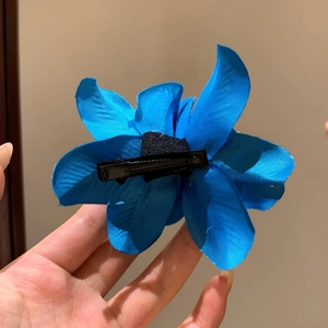 Vista dettagliata del retro di una clip per capelli a fiore blu con molletta nera.