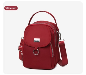 Detail view of wine red nylon crossbody bag featuring triple zipper compartments and strap