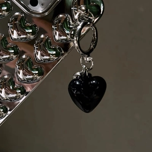 Close-up of a glossy black resin heart pendant attached to a silver metal heart phone case