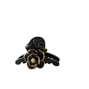 Mini black camellia hair claw clip with gold edges and pearl center on white background