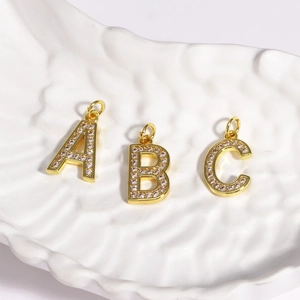 Detail of three gold zircon letter A B C pendants in a white shell display tray