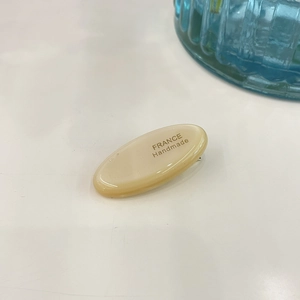 Handmade cream oval hair clip with France Handmade engraving on white surface