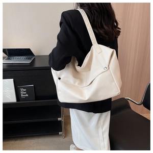 Detail of cream tote bag featuring textured leather, woven strap and rivet accents