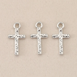 Macro shot of silver baroque cross pendants with hammered texture on beige fabric