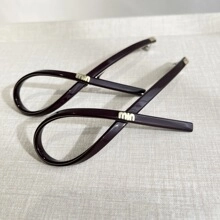 Détail de pinces à cheveux en acétate brun rouge avec logo min doré sur tissu beige