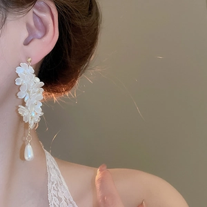 Close-up of elegant flower petal earrings with pearl droplets worn by a model