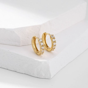 Macro shot of gold S925 silver hoop earrings with pavé zircon on white stone surface