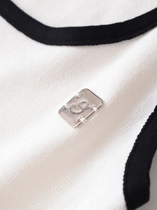 Makrodetail aus weißem Strick mit schwarzem Saum und silberner Logo-Plakette