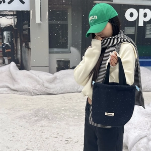 Detail of black polka dot wool drawstring handbag with brand label in winter outdoor setting