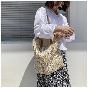 Detail of woven straw shoulder bag with brown leather handles and X-stitch reinforcement