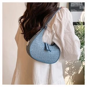Detail of blue woven shoulder bag texture shown on model in a warm interior setting