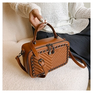 Dettaglio borsa a scatola in pelle marrone con motivo a V e catena decorativa